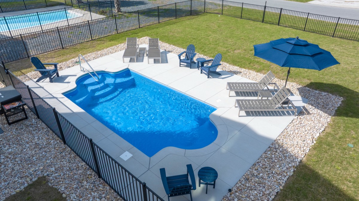 Fenced backyard pool with lounge chairs and umbrella